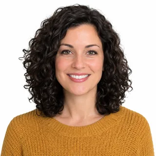 Chest-up photo of a curly-haired woman in a mustard sweater smiling at the camera on a white background