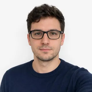 Chest-up photo of a man in clear, dark-rimmed glasses looking at the camera, white background