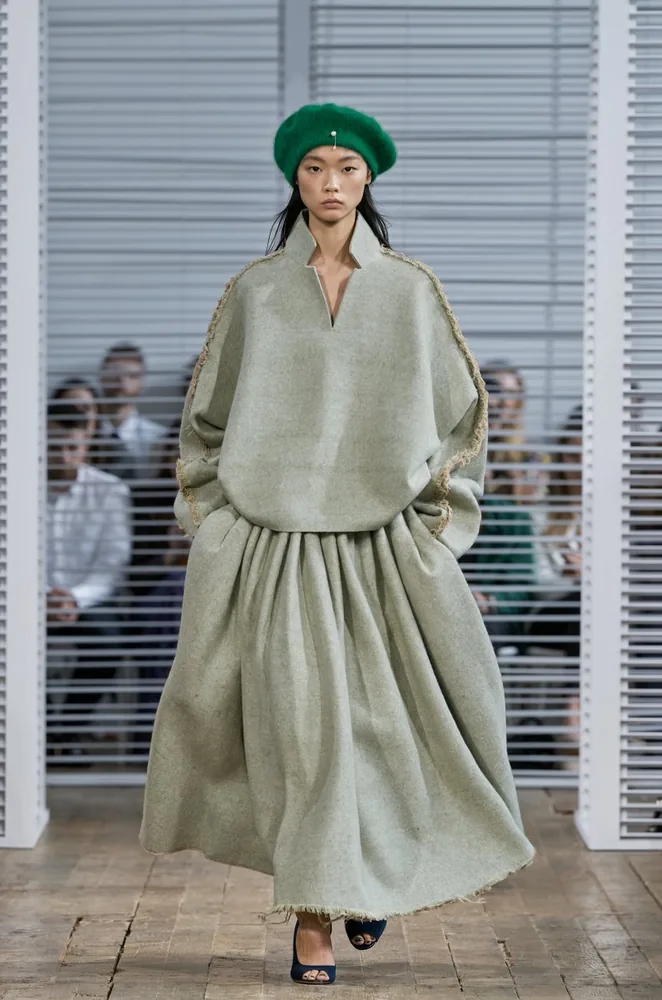 Fashion portrait of a woman in a green beret and a loose grey-green outfit outside a storefront.