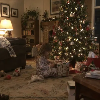 A child in pajamas playing with a gift by the Christmas tree in a living room