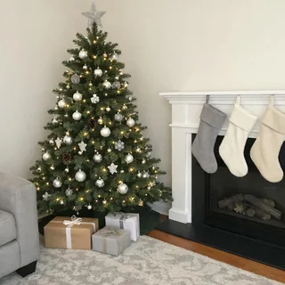 An empty living room corner with a decorated tree, wrapped gifts and stockings on a white fireplace