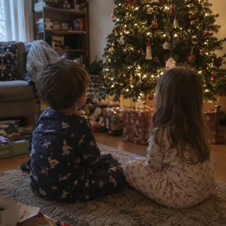 Two children in pajamas sitting by a Christmas tree