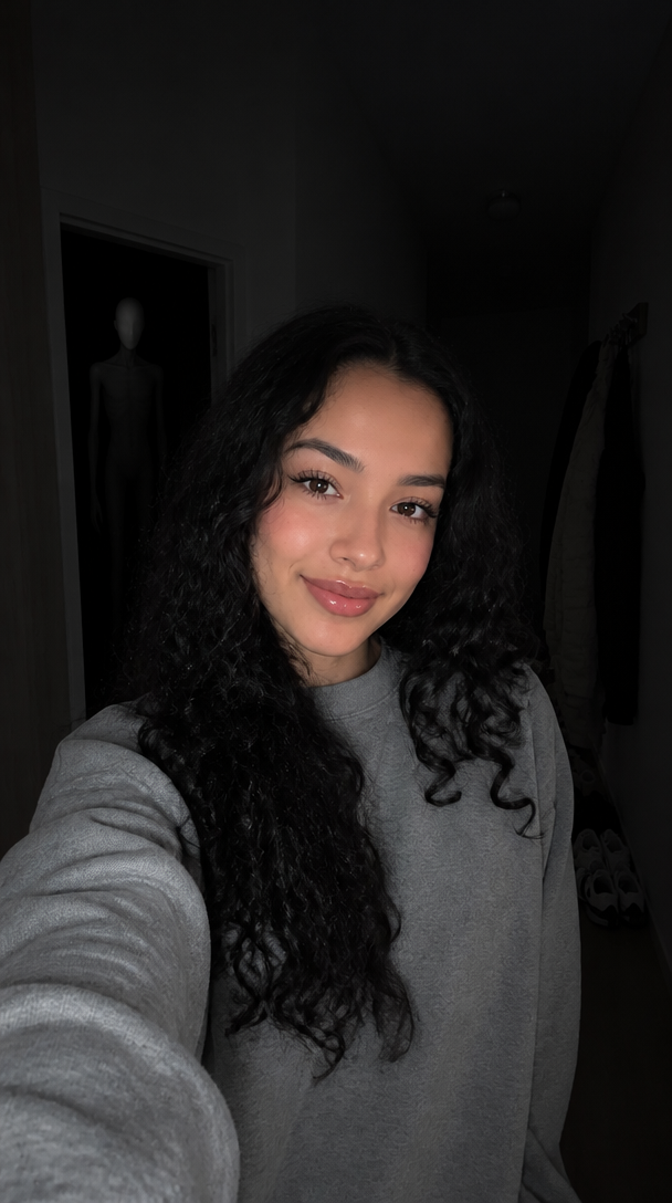 A dim hallway selfie of a smiling woman with a tall faceless shadow figure in the doorway behind her