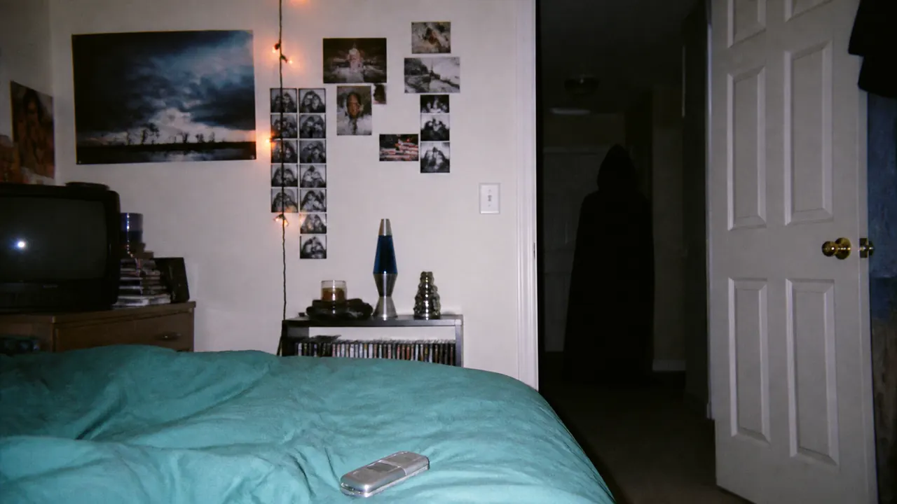 A flash-lit 2000s bedroom with a flip phone on the bed and a faceless hooded figure standing in the dark doorway