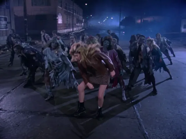The lead bent forward at the waist with her blonde hair flung down, zombie dancers bending around her