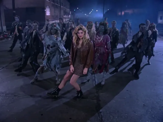 The lead kicks one foot out to the side on the asphalt, the zombie crowd spread across the street behind her