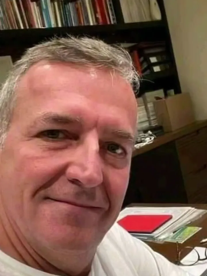 A grey-haired man's selfie at his desk, bookshelves behind him