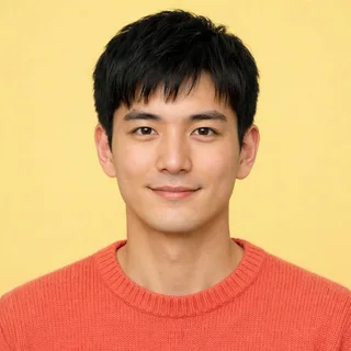 A young man with short black hair smiling straight at the camera against a yellow backdrop
