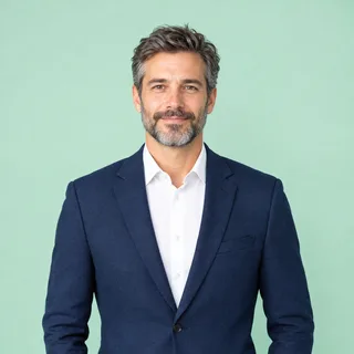 A bearded man in a navy blazer shown from the waist up in even light against a mint backdrop