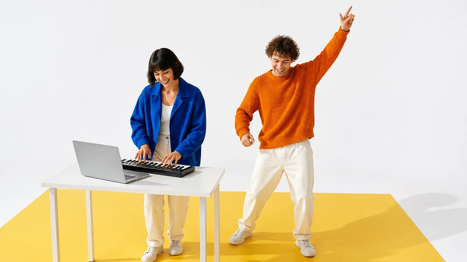 Two friends in a white studio, one playing a small keyboard on a laptop while the other dances with an arm in the air