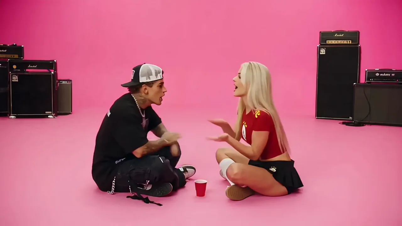 A man and a woman sitting cross-legged on a pink floor, clapping hands over a red cup