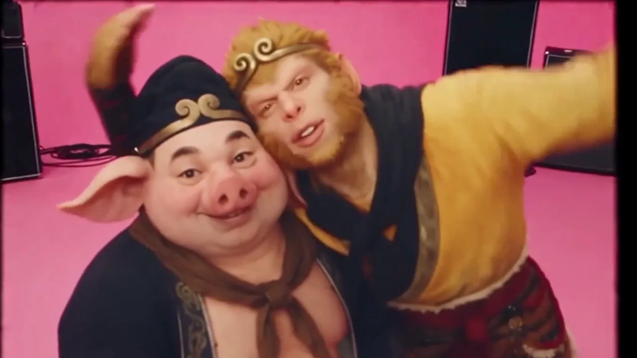 Two costumed performers taking a close selfie in a pink studio, one with pig ears and one with a golden headband