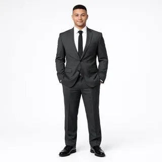 A young man in a charcoal suit, tie and black dress shoes, photographed head to toe on a white background