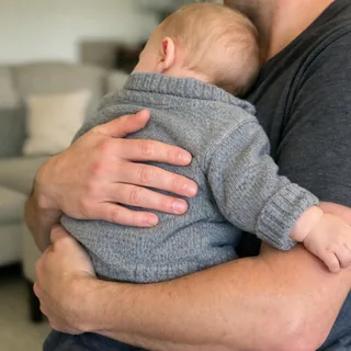 Adult hands and forearms holding a baby against a chest, the baby turned away