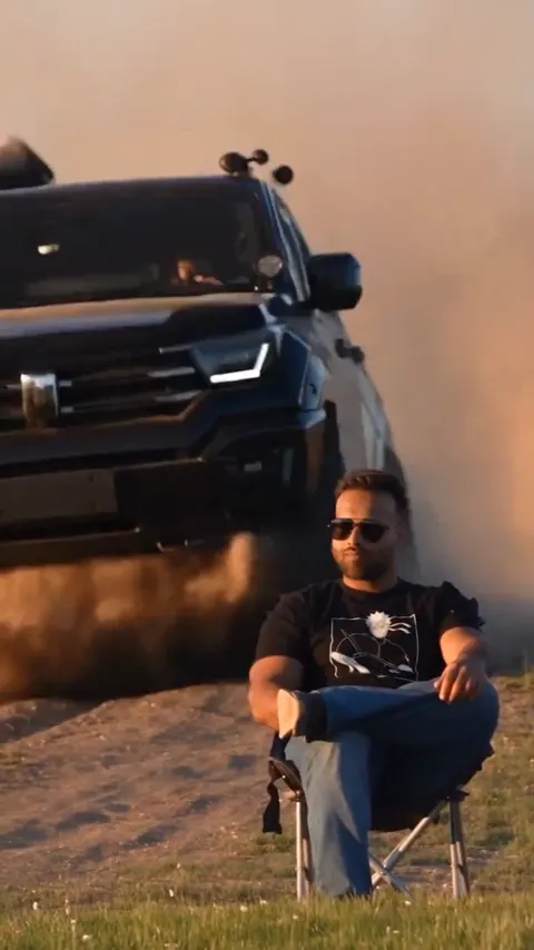 SUV 落在椅子后方，穿过尘土开过，男人仍坐着不动