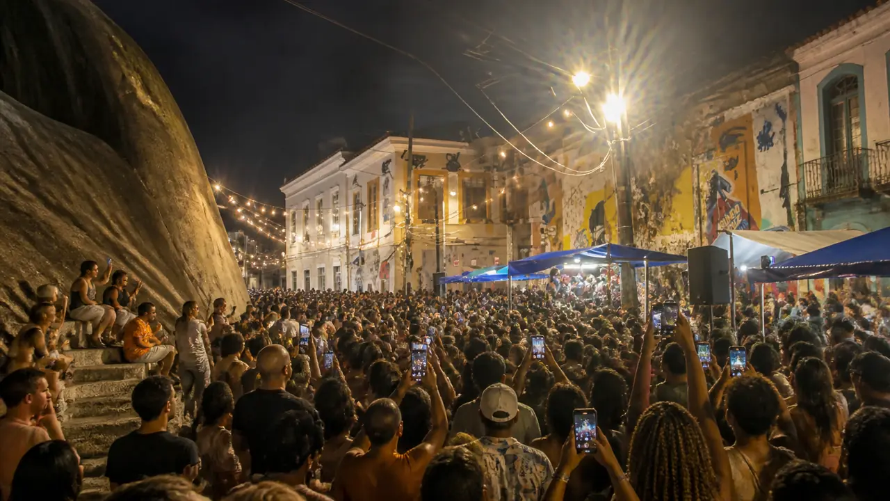 Illustration: a night street party in an old Rio square, a granite rock with carved steps on one side, painted colonial houses and string lights above a crowd holding up phones.