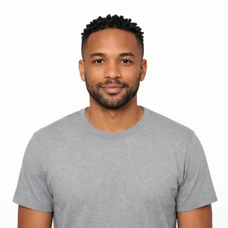 A man with short twists and a beard looks straight into the camera on a plain white background, his face evenly lit.