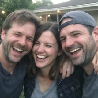 Three friends squeezed shoulder to shoulder, faces close together, at a blurred backyard gathering.