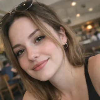 A tilted close-up selfie of a woman in a café, only her face and one shoulder in frame.