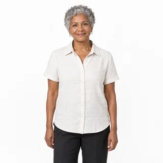 A grey-haired woman in a linen shirt stands facing the camera on a plain white background, framed from the thighs up.