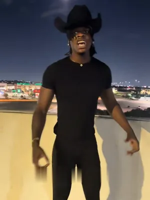 The singer in a black cowboy hat and all black walking toward the camera on the rooftop