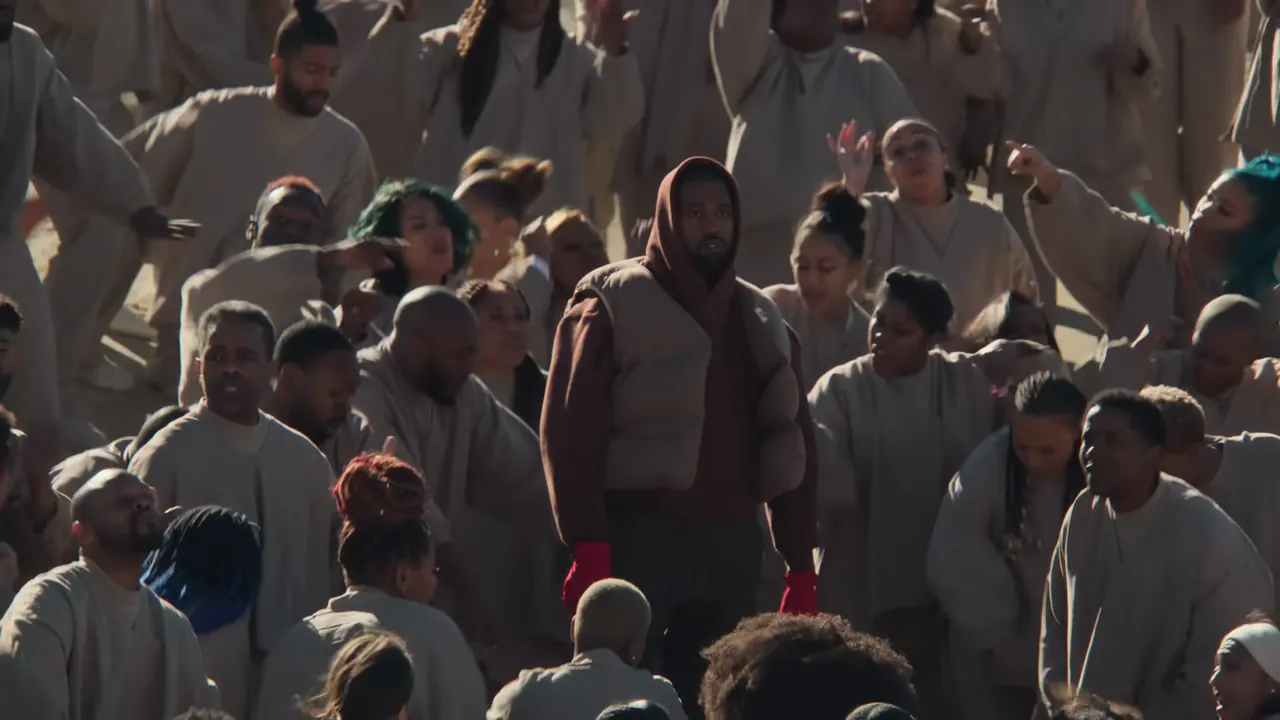 The camera pulls back and more rows of robed singers appear around the still figure