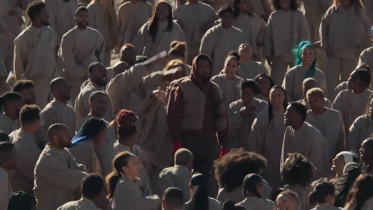A wide frame of the full choir on the hillside with one unmoving figure in the middle