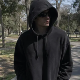 Snapshot of a man in dark sunglasses and a pulled-up hood in a park