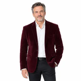 A man in a burgundy velvet blazer photographed knees up on a white background