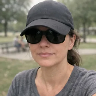 A woman in sunglasses and a low baseball cap in a park