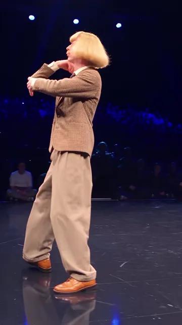 Dancer leaning back with a hand at his mouth, face turned up to the lights