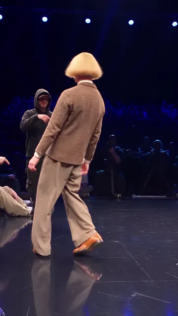 Dancer with his back to the camera while the hooded opponent watches from behind