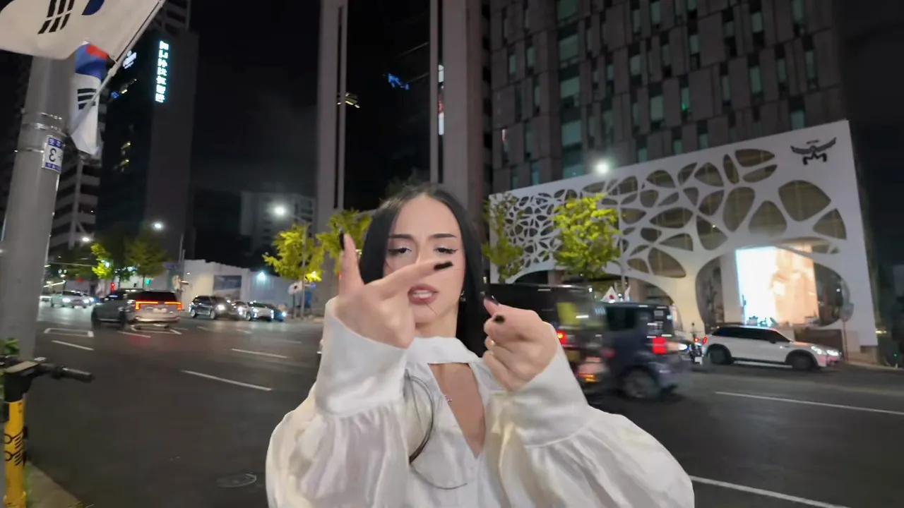 江南的夜街：路灯杆上挂着太极旗，车流和镂空外立面的大楼前站着一位穿白衬衫的女生