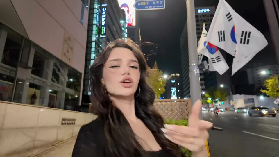 深色卷发的女生指着镜头，身后旗杆上飘着太极旗