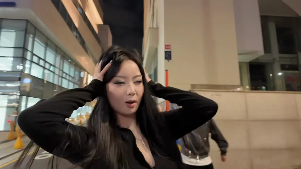 穿黑衣的女生在玻璃写字楼旁的人行道上双手撩起长发
