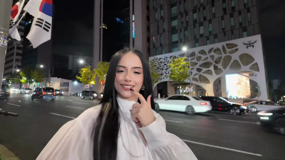 穿白衬衫的女生在夜晚车流旁托着下巴，身后是镂空外立面的大楼