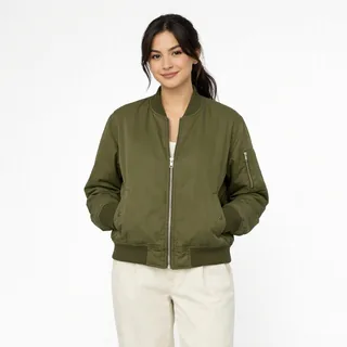 A young woman in an olive bomber jacket and cream trousers, standing from the knees up on a white background