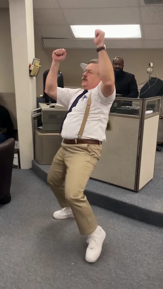 The dancer finishing in a wide squat with both fists raised in front of the coworkers