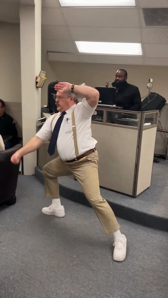 The dancer in a low side lunge with one hand at his head as a coworker crosses the foreground