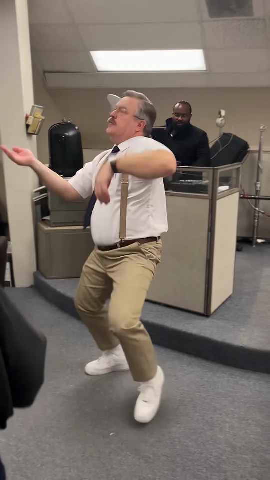 One arm swept out to the side as the dancer half-turns with coworkers behind the counter