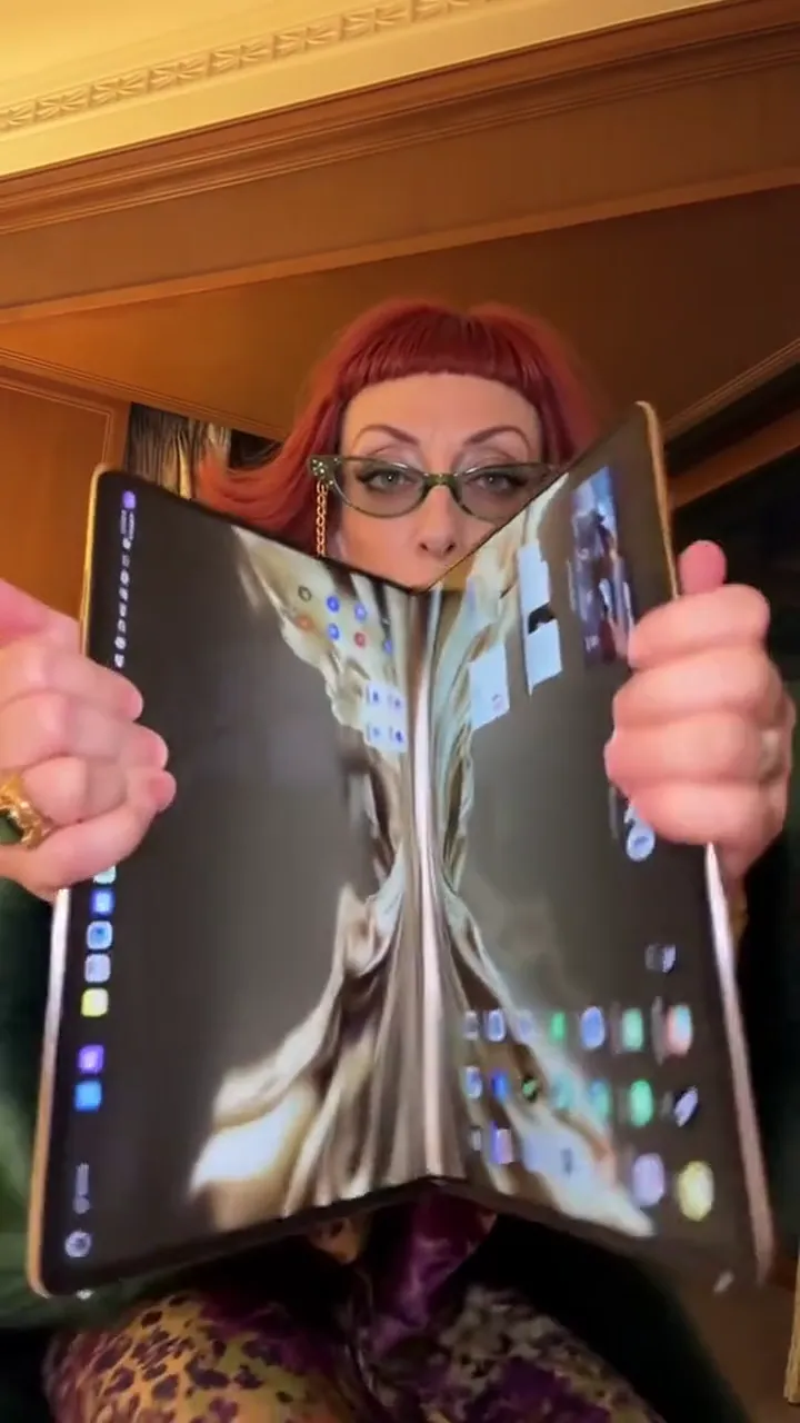 A foldable phone held open toward the lens, the inner screen bright against a dark room
