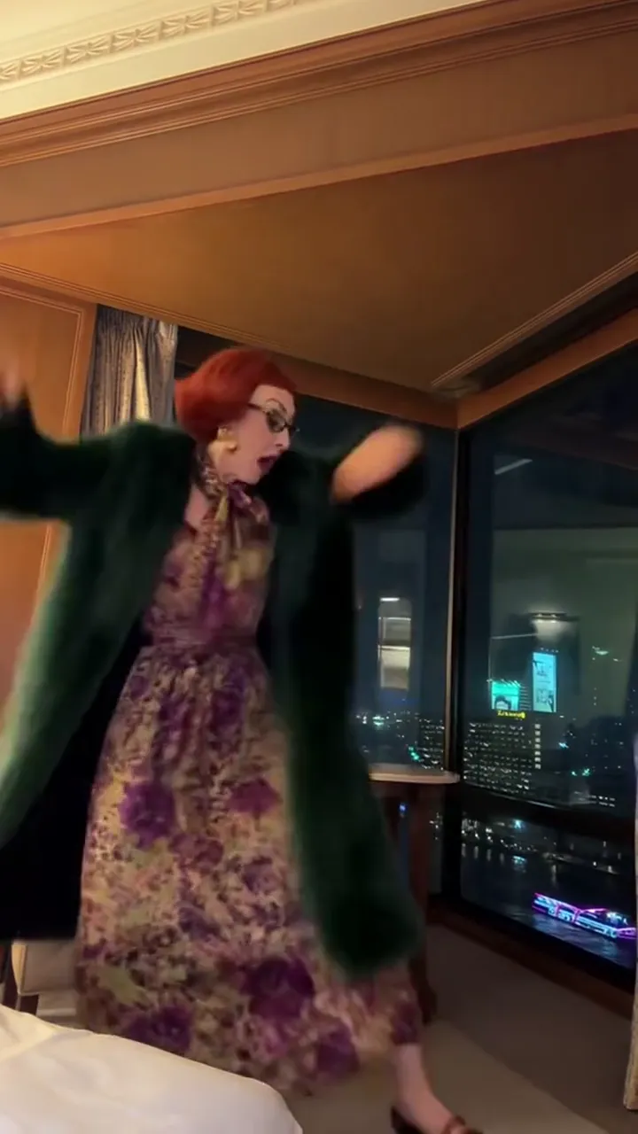 A foldable phone in the air above a hand in a hotel room, the room blurring behind it