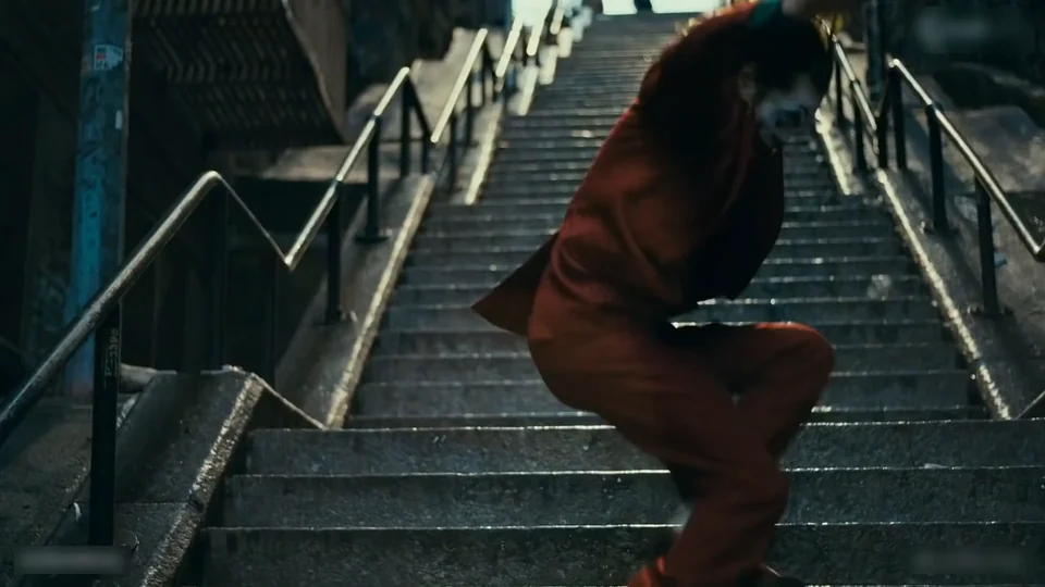 The dancer walking down the steps on a diagonal with both arms open, seen from below in the long shot