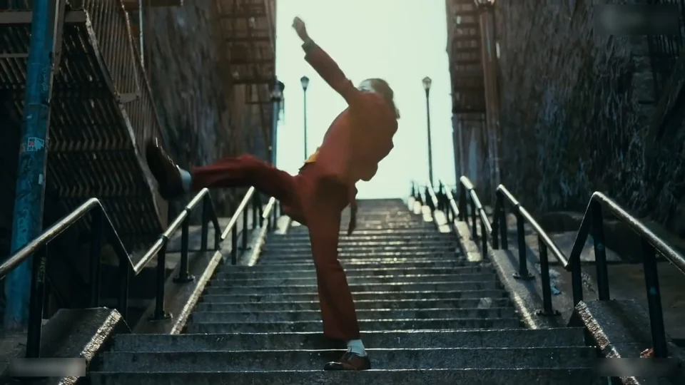 A dancer in a red suit kicking one leg out at the top of a long outdoor staircase