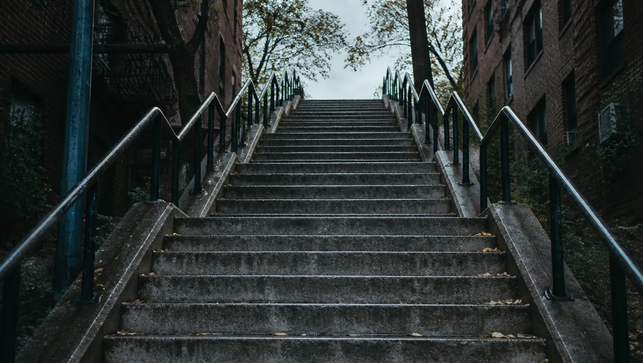 A long grey concrete staircase climbing between brick apartment blocks on an overcast day, nobody on the steps