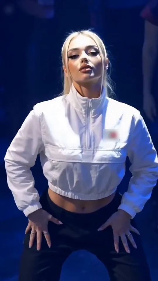 The spotlight dancer stands in white light on a blue dance floor and looks up toward the balcony