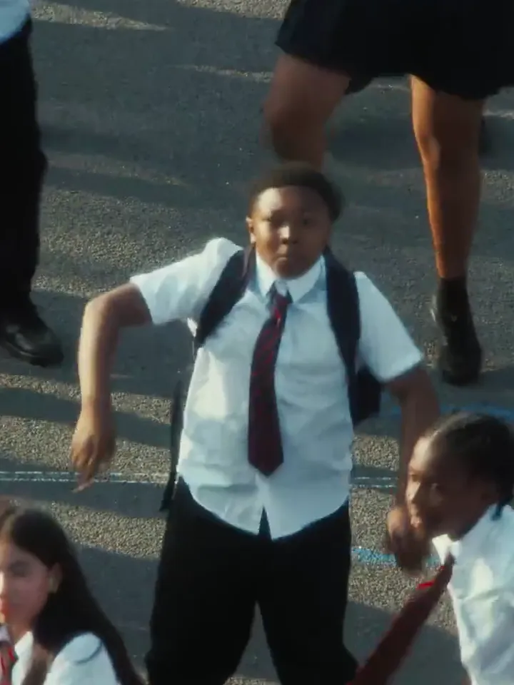 The lead dancer in a white shirt, striped tie and backpack, at the centre of the playground crowd