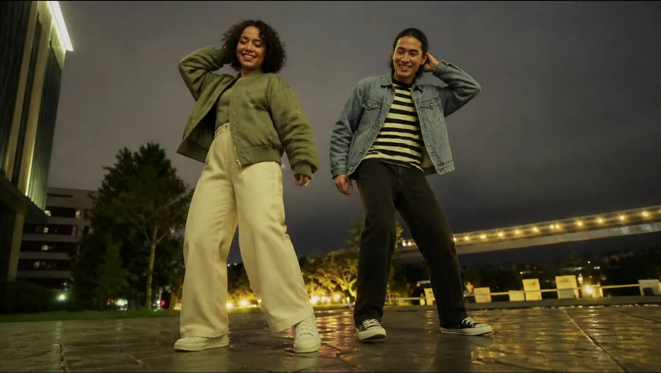 Low-angle night shot of two friends in a green bomber jacket and a denim jacket dancing side by side on a plaza