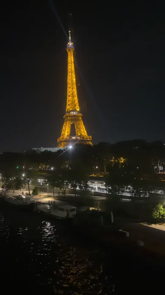 The lit Eiffel Tower at night above the Seine, seen through the window of a metro car