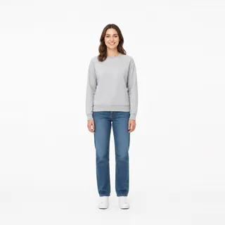 A woman in a grey sweatshirt and jeans on a white background, in frame from head to sneakers
